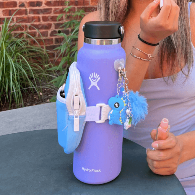 Person holding a purple Hydro Flask with a blue dragonfly keychain outdoors.
